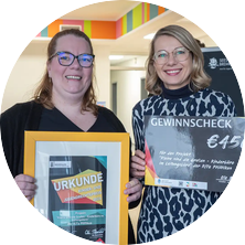 Das Foto zeigt zwei Frauen. Sie halten einen Gewinnscheck und eine Urkunde in ihren Händen.